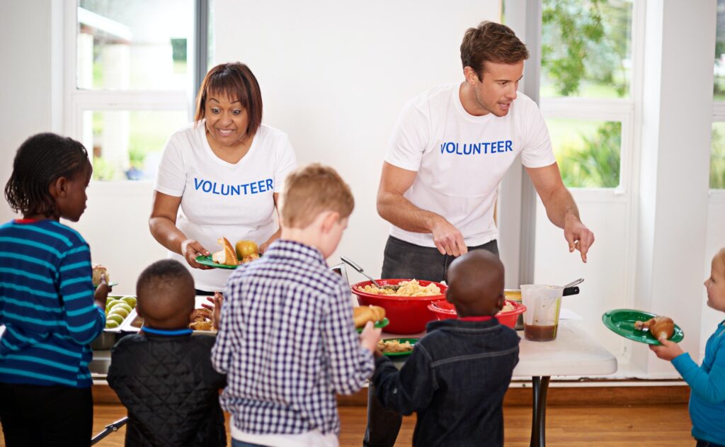 Generosity keeps giving. Shot of volunteers serving food to a group of little children.