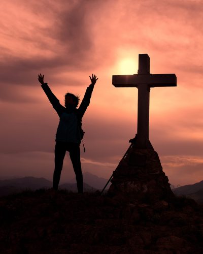 Cross at the top of the mountain with a mountaineer who raises his hands